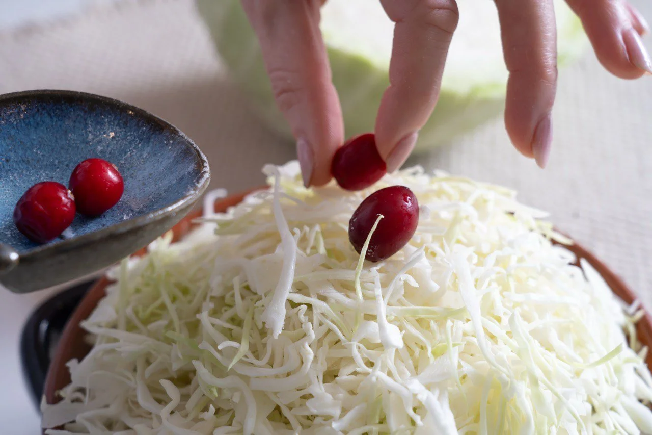 Person placing small red radishes onto shredded cabbage in a bowl.