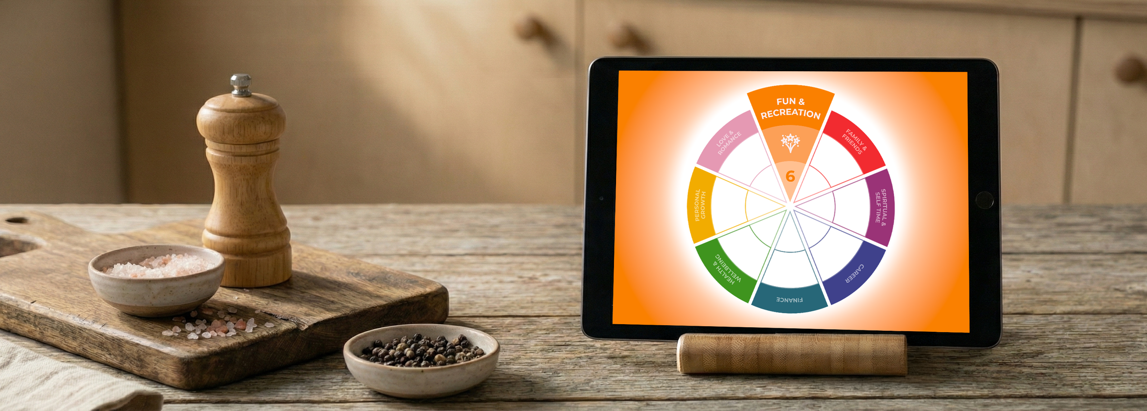 Tablet on a wooden table displaying a colorful wheel diagram labeled with various categories like Fun & Recreation, Love & Romance, Personal Growth, etc. Nearby are bowls of pink Himalayan salt, peppercorns, and a salt grinder.