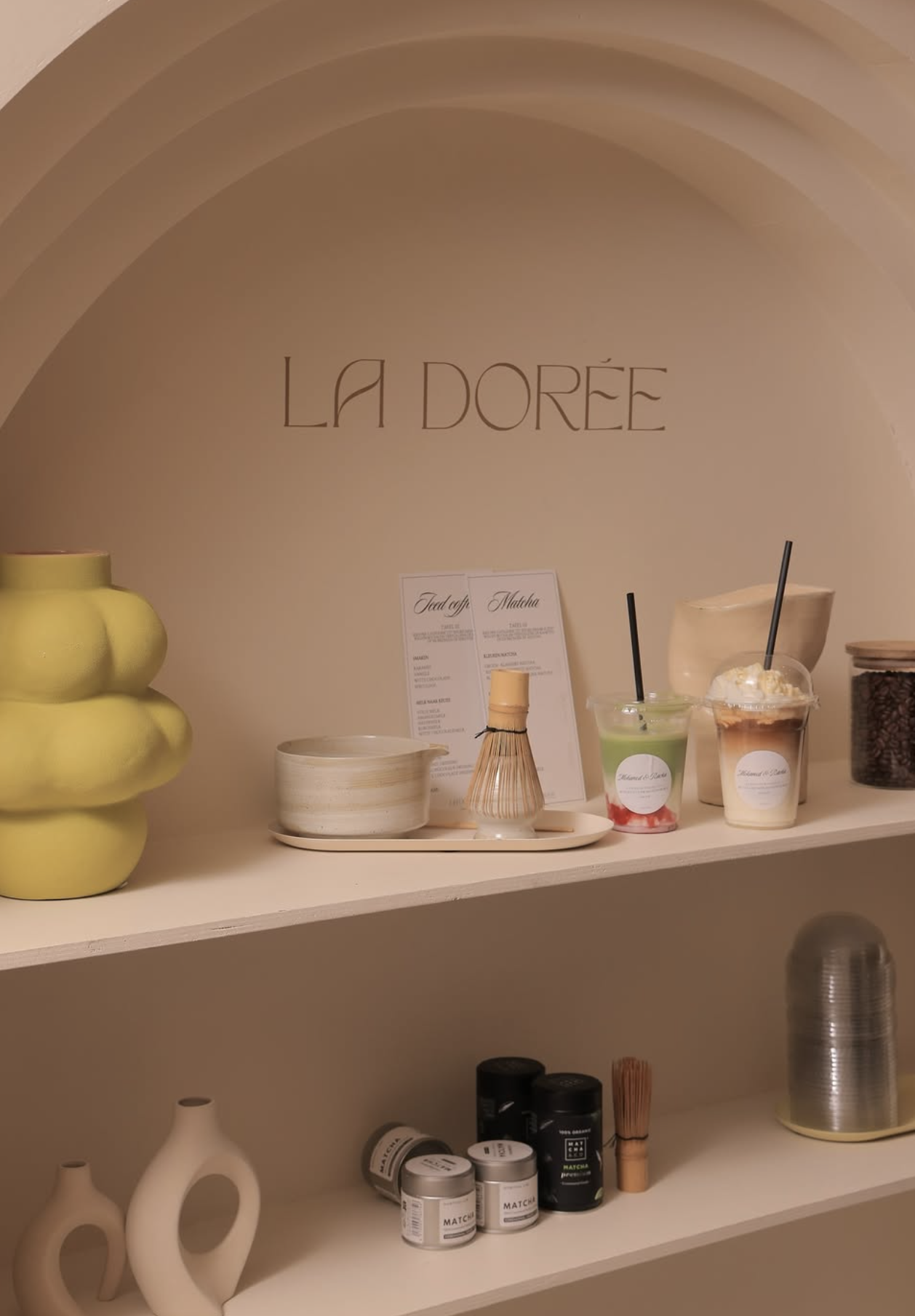 Schoonmaakplanken met decoratieve vazen, koffie- en theeproducten, en smoothies in een minimalistische sfeer in een ruimte met de tekst 'LA DOREE'.