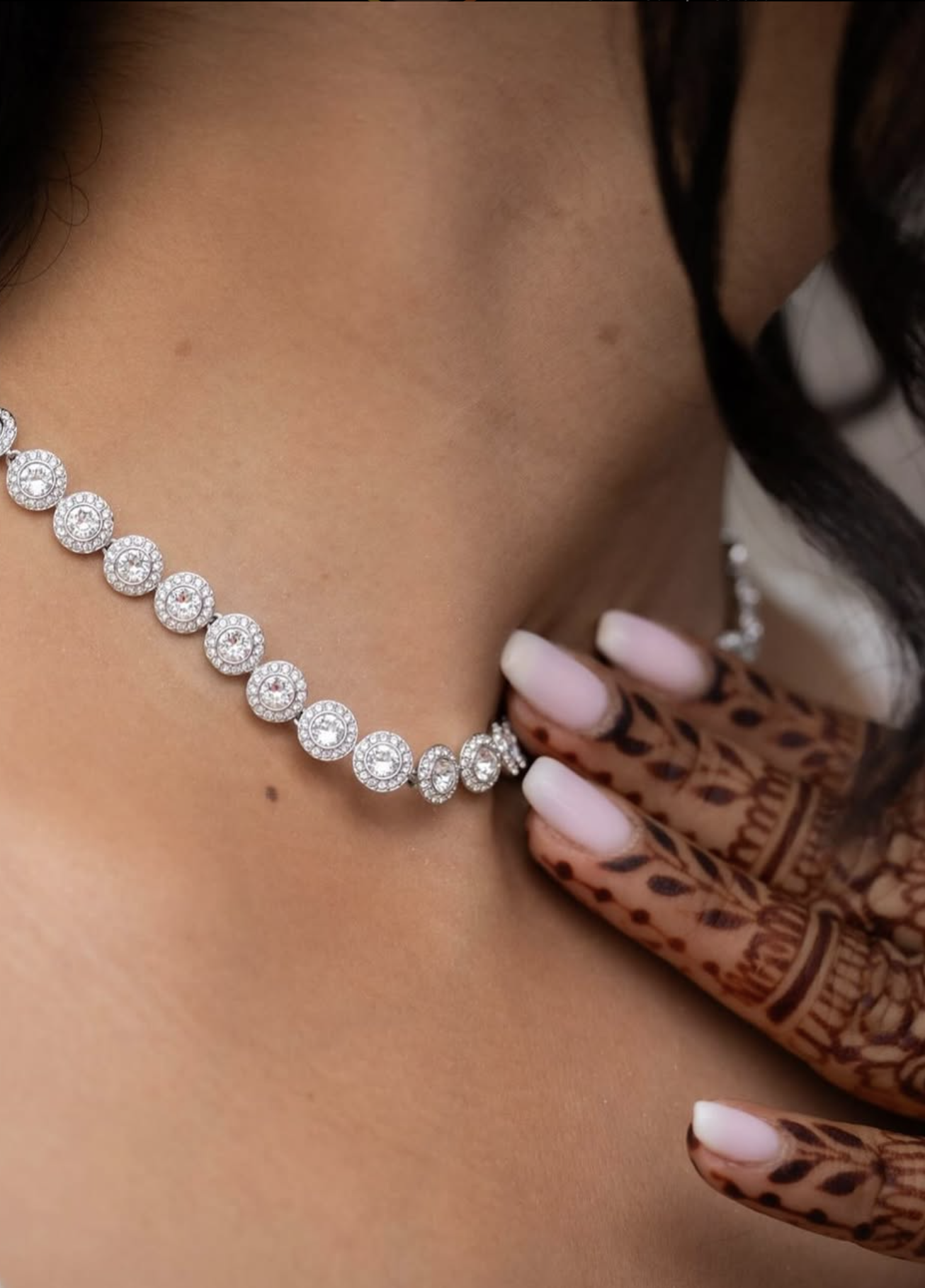 Close-up van een vrouw die een sieradenset draagt, bestaande uit een glanzende, ronde parelketting en een ring, met langdurige nagellak en een hand met henna-tatoeages.