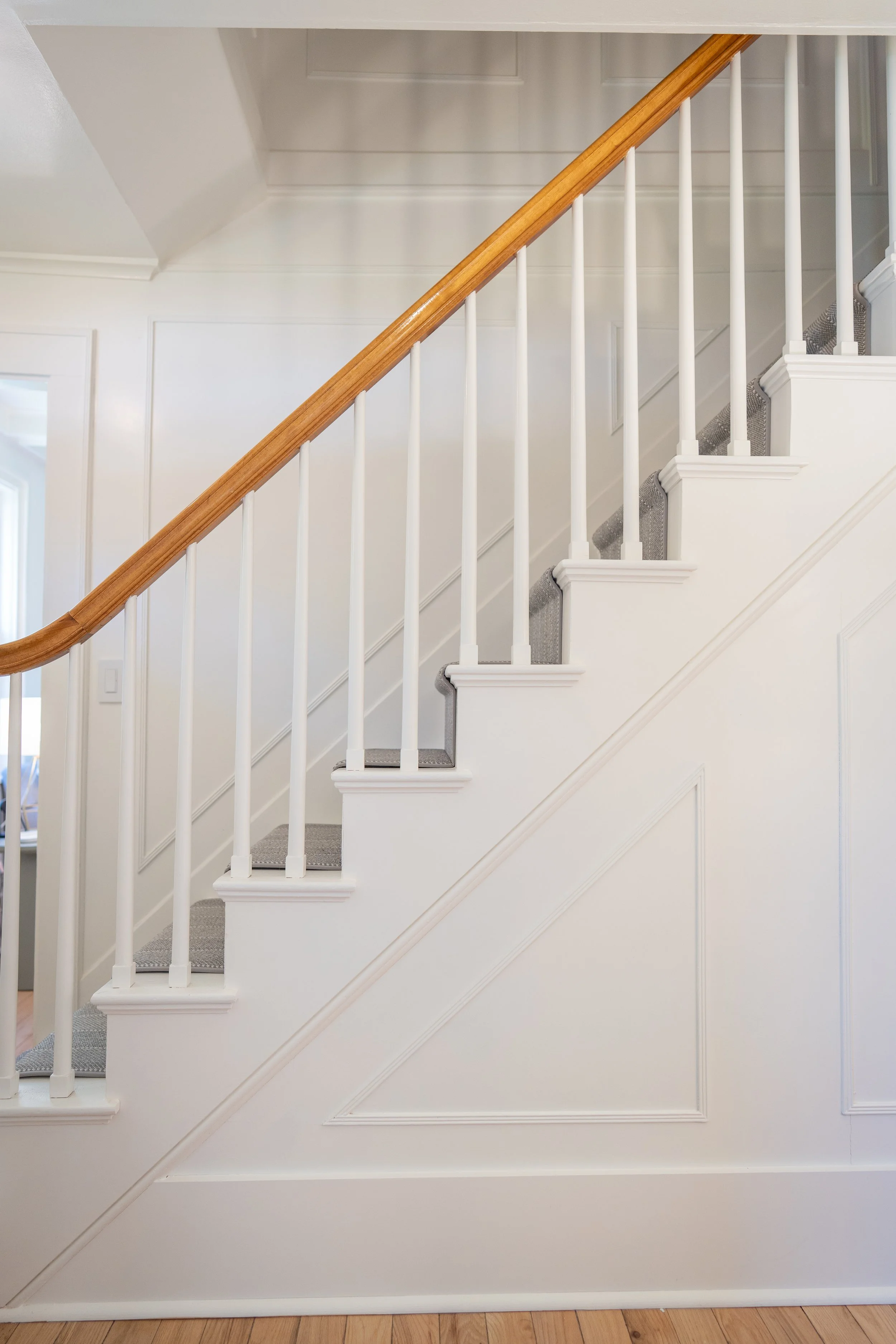 Interior view of a staircase with white walls, wooden handrail, and gray carpeted stairs.
