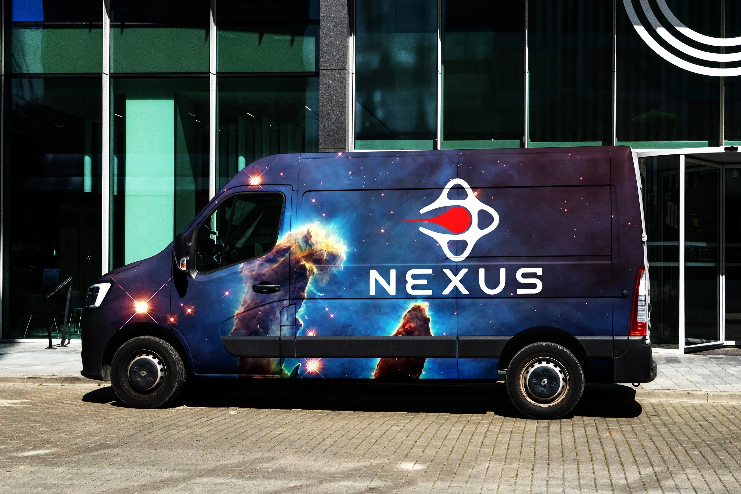 A delivery van parked on a brick sidewalk in front of a modern glass building. The van features a space-themed design with nebulae and stars, and displays the logo and name 'NEXUS'.