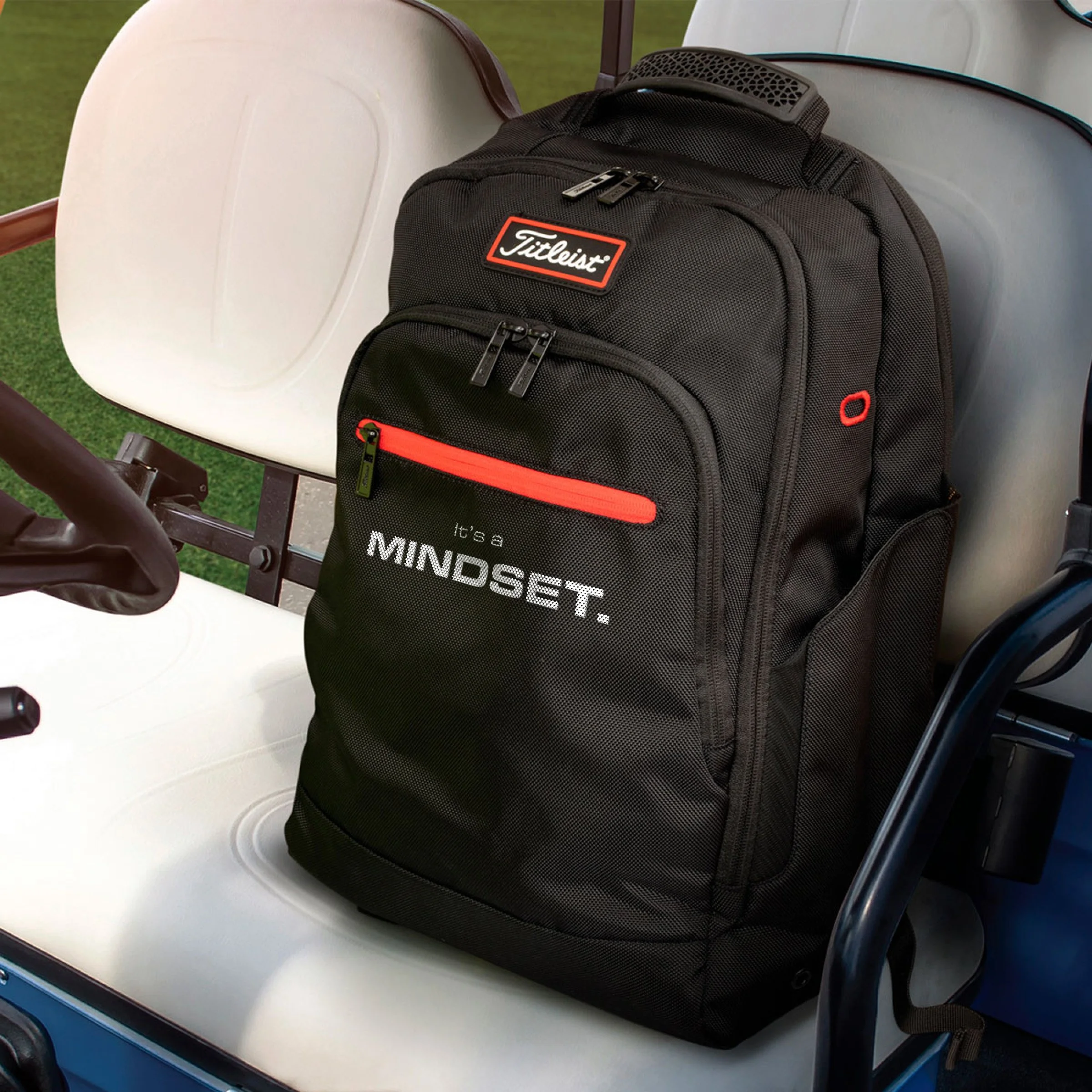 A black Titleist golf bag with red accents and the text 'it's a MINDSET.' on it, sitting on a golf cart seat.