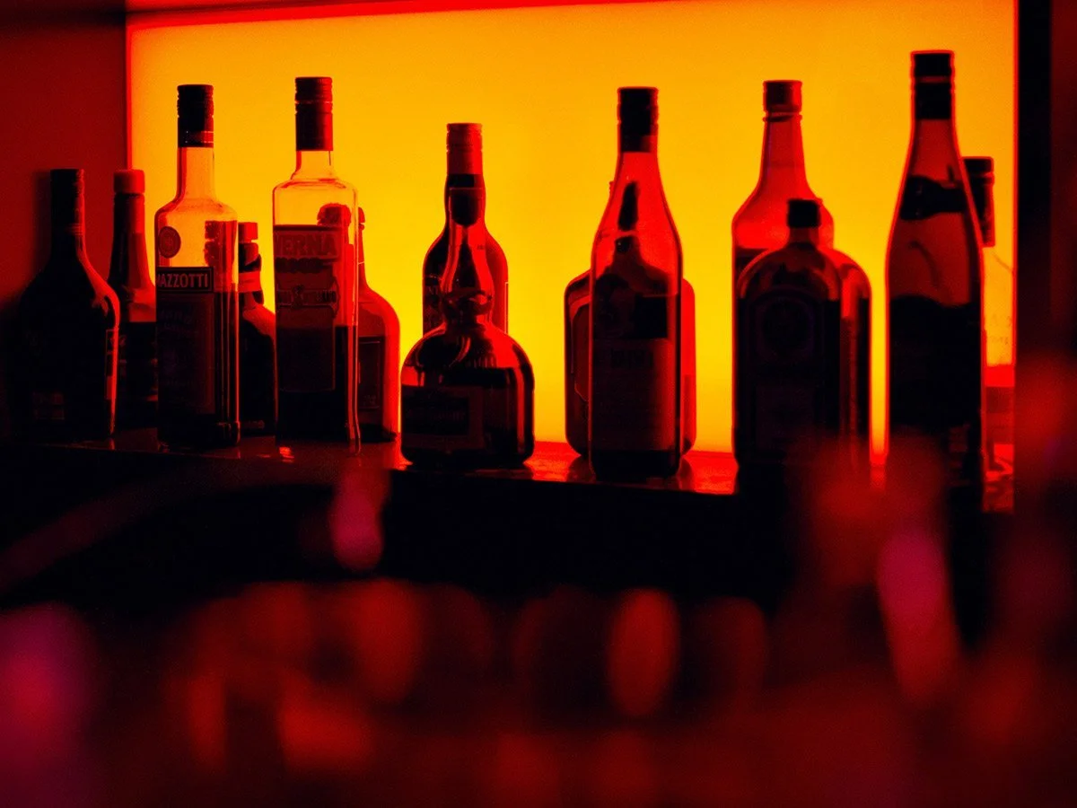 Silhouette of various liquor bottles on a bar counter against a vibrant orange backlit background.