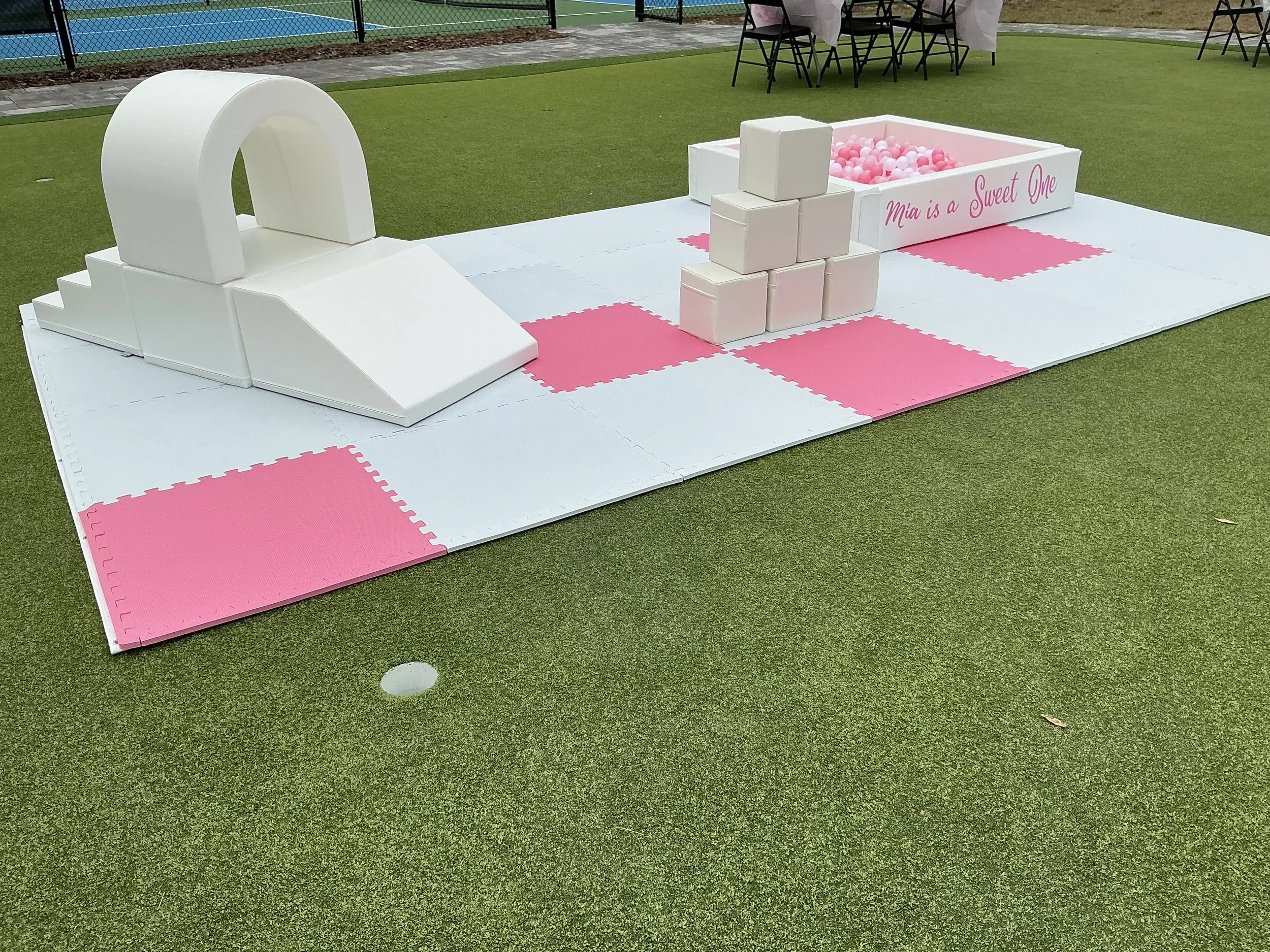 Inflatable white canopy bed set up outdoors on a grassy lawn, with greenery and trees in the background, decorated with flowers and plants.