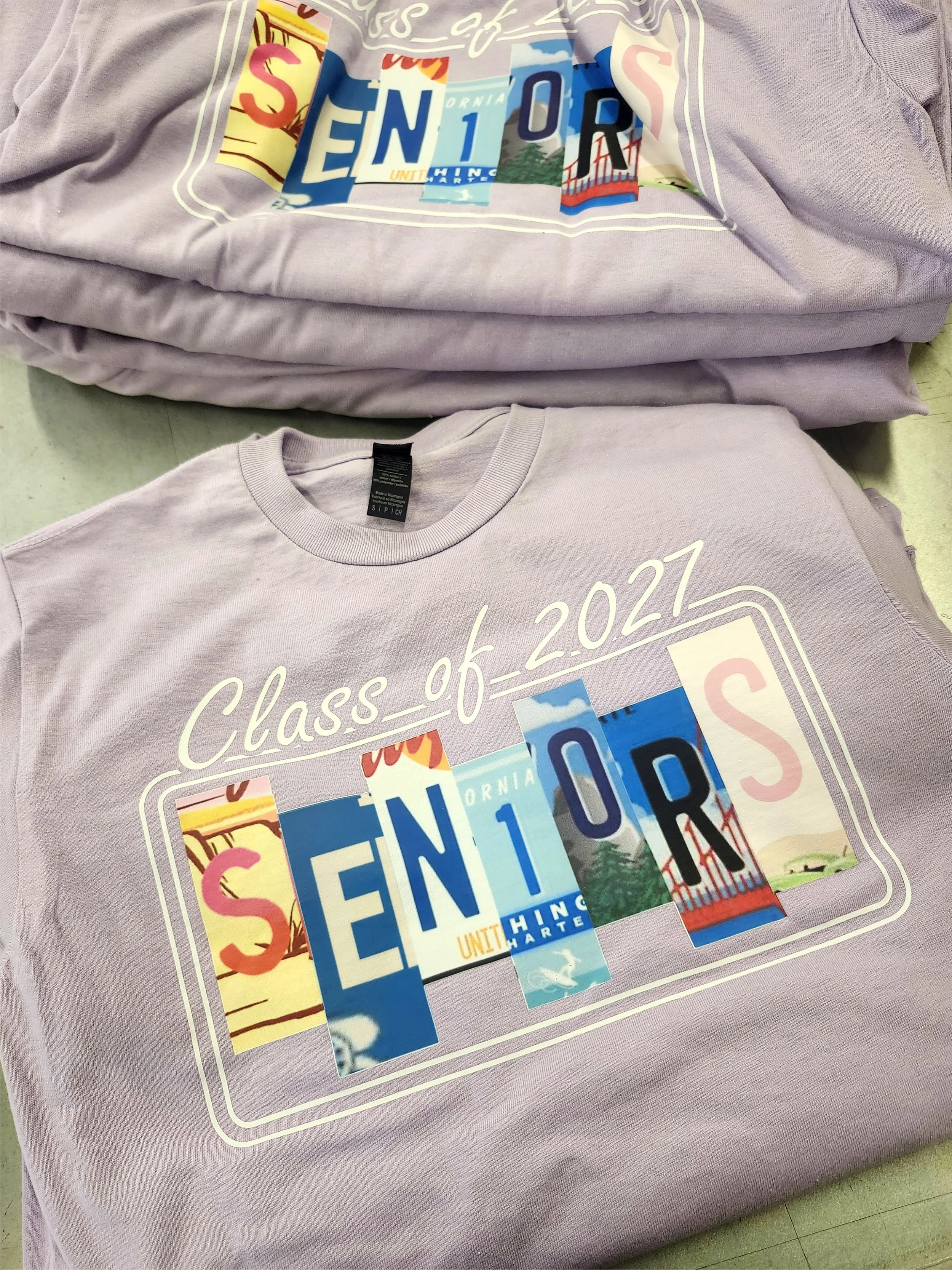 A purple DTF  T-shirt with a colorful graphic design that includes the words 'Class of 2027'  The design features cut-out letter images of various license plates and scenic images.
