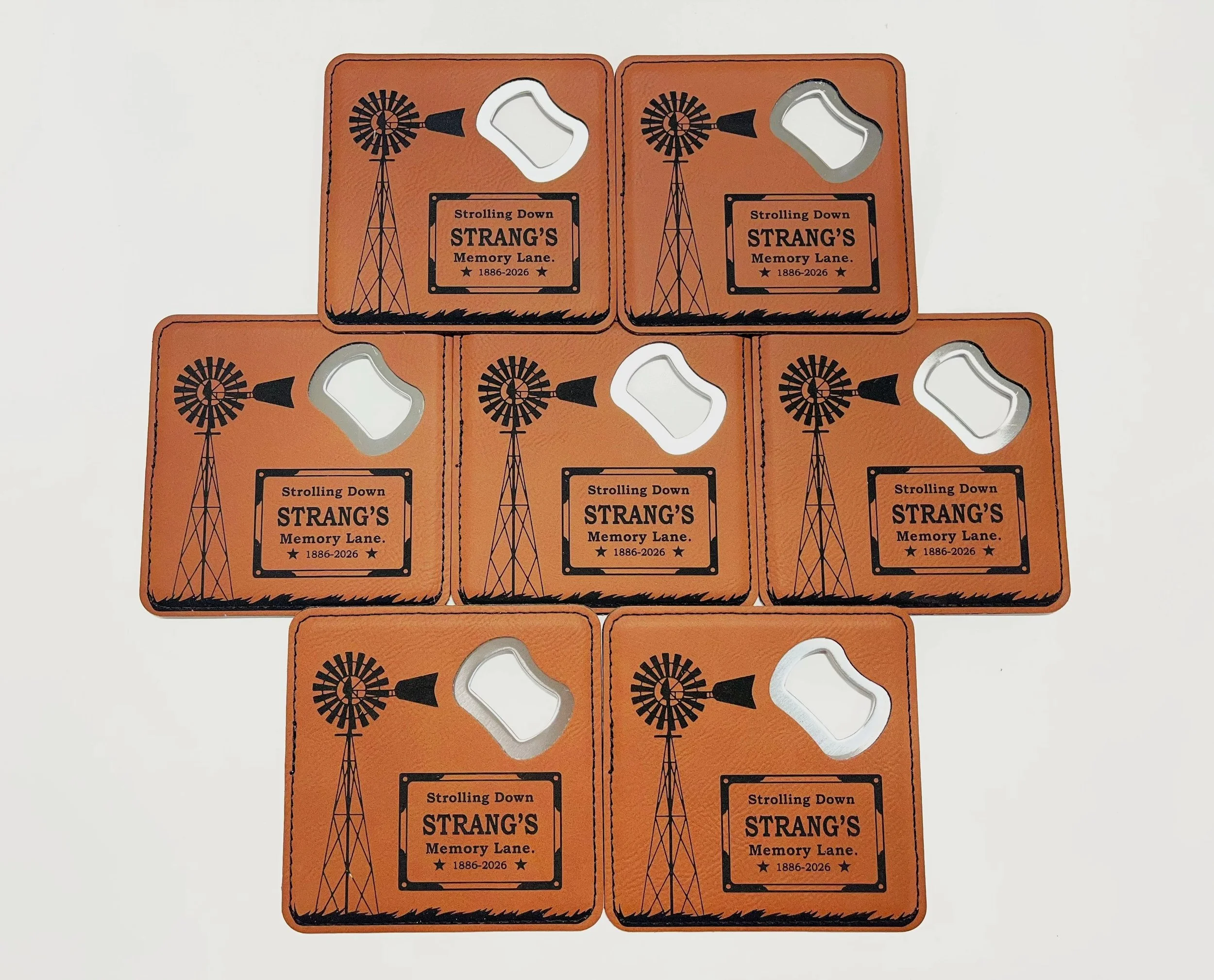 A group of rawhide coasters  with a windmil design, reading 'Strolling Down STRANG'S Memory Lane. 1886-2026'.