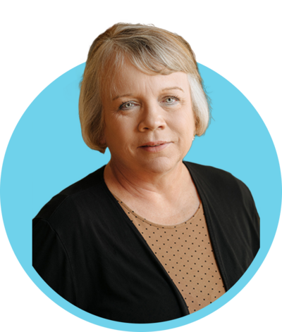 A middle-aged woman with short blonde hair wearing a black cardigan over a tan polka dot top, looking at the camera with a neutral expression.
