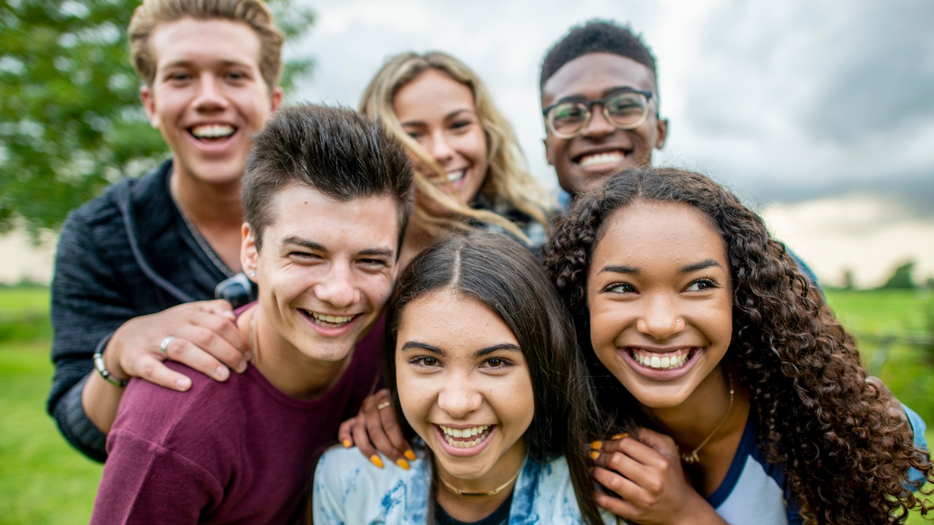 Group of six young people smiling and posing outdoors in a park.