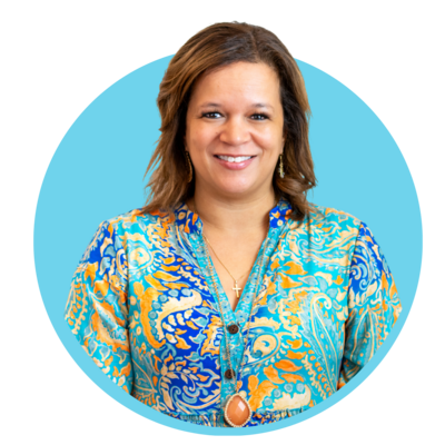 Smiling woman with shoulder-length brown hair wearing a colorful patterned blouse and necklace, against a blue background.