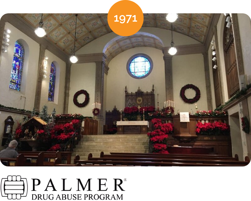 Inside a church decorated with red poinsettias and wreaths for Christmas, with stained glass windows and an altar in the background.