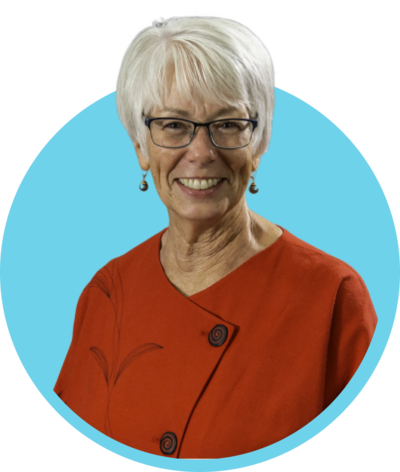 An elderly woman with short white hair and glasses, smiling, wearing an orange top with a floral design, against a blue circular background.