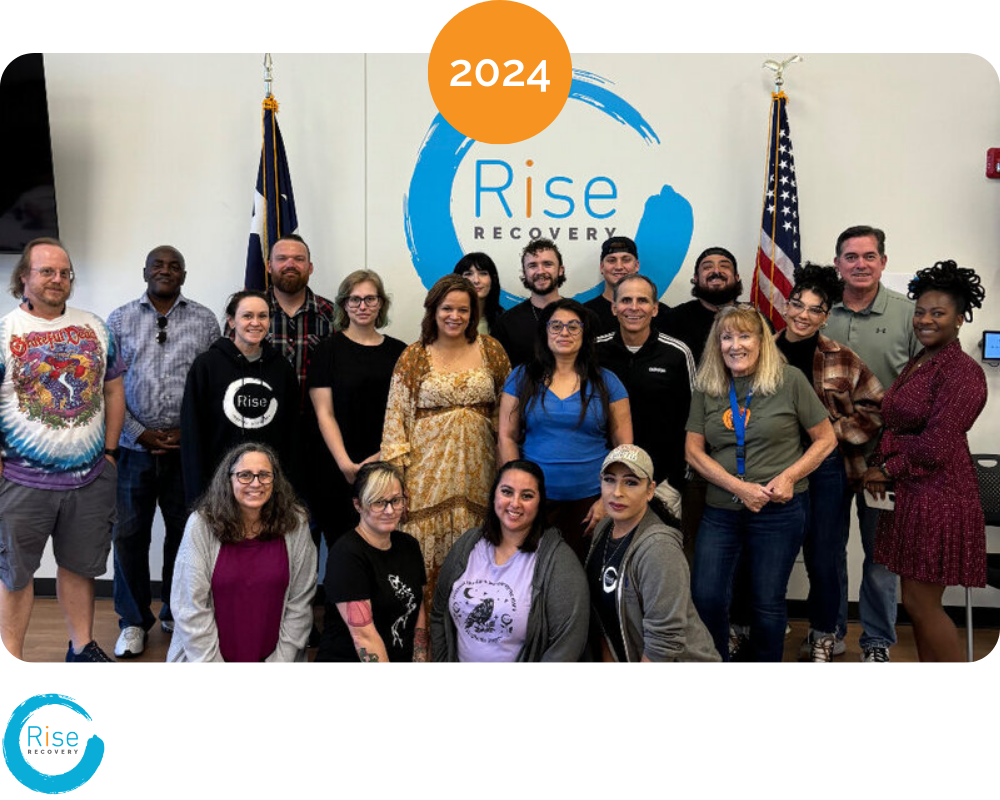 Group of diverse people standing in front of a wall with the 'Rise Recovery 2024' logo, American flags on either side, smiling and posing for the photo.