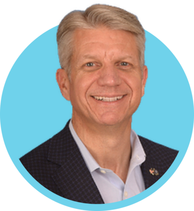 A smiling man in a suit with a light blue background.