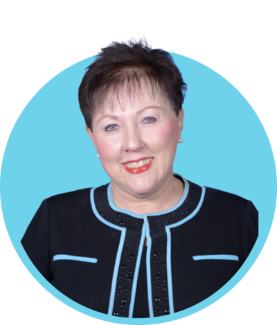 A woman with short brown hair and light makeup, wearing a black jacket with light blue accents, smiling against a light blue background.