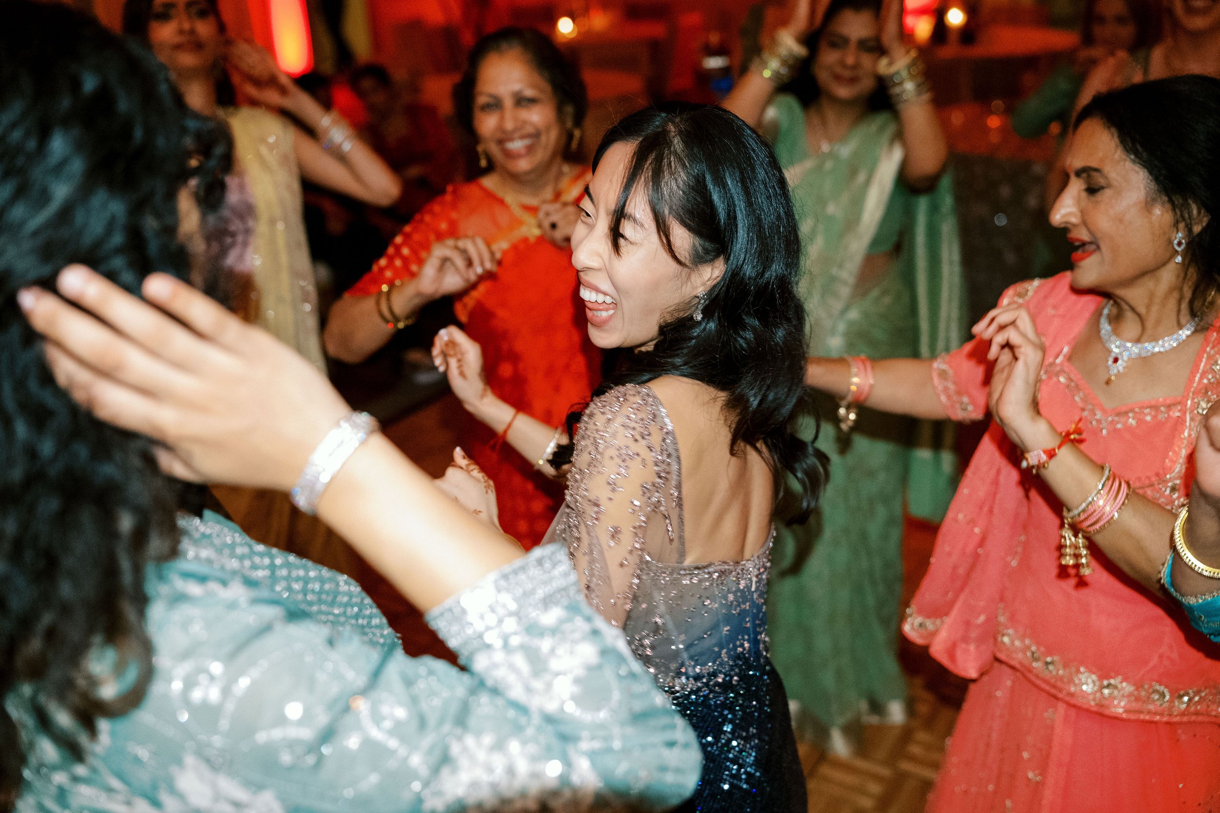 Group of women dancing and celebrating at an indoor event, dressed in colorful traditional attire.
