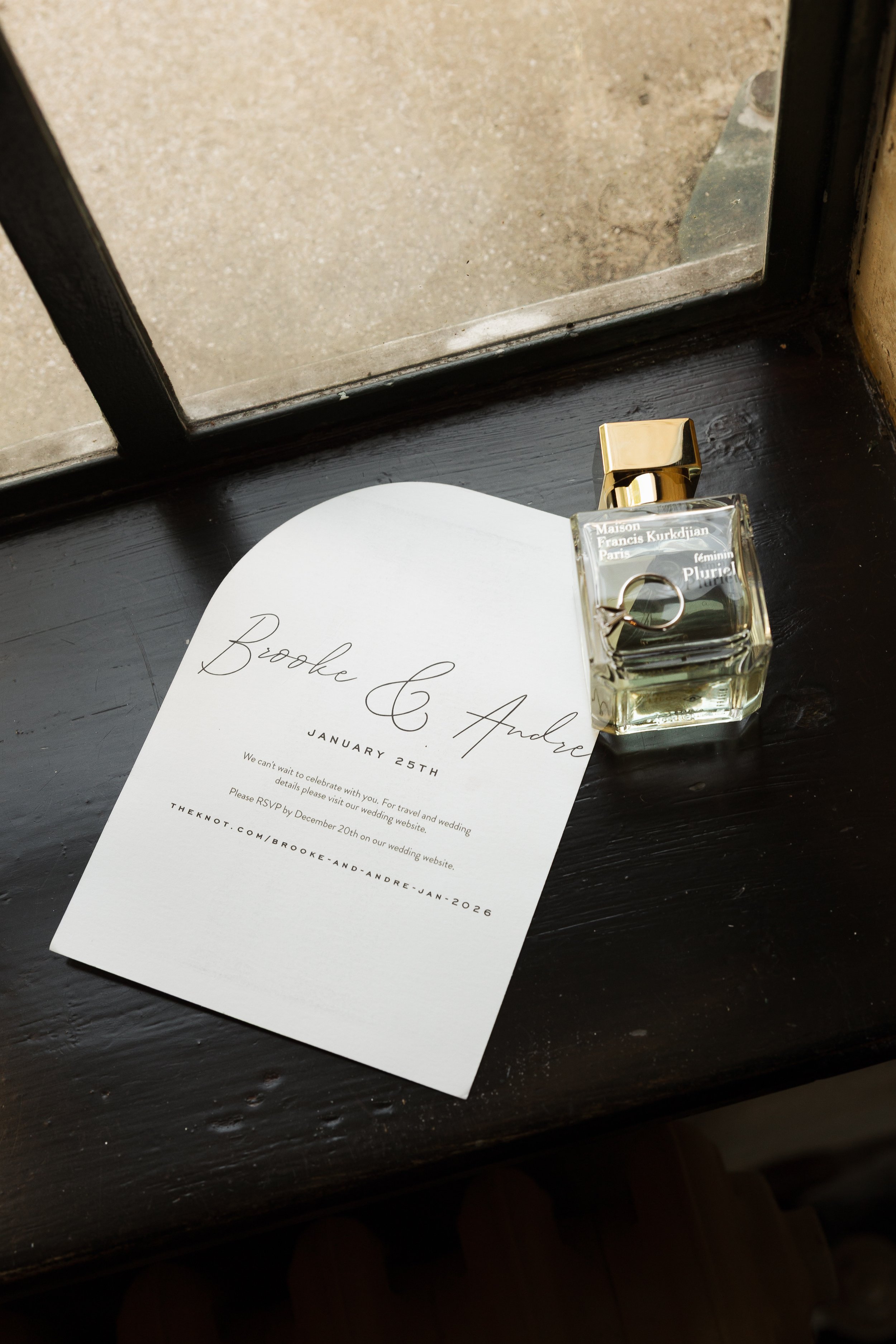 Wedding RSVP card and perfume bottle on a dark windowsill.