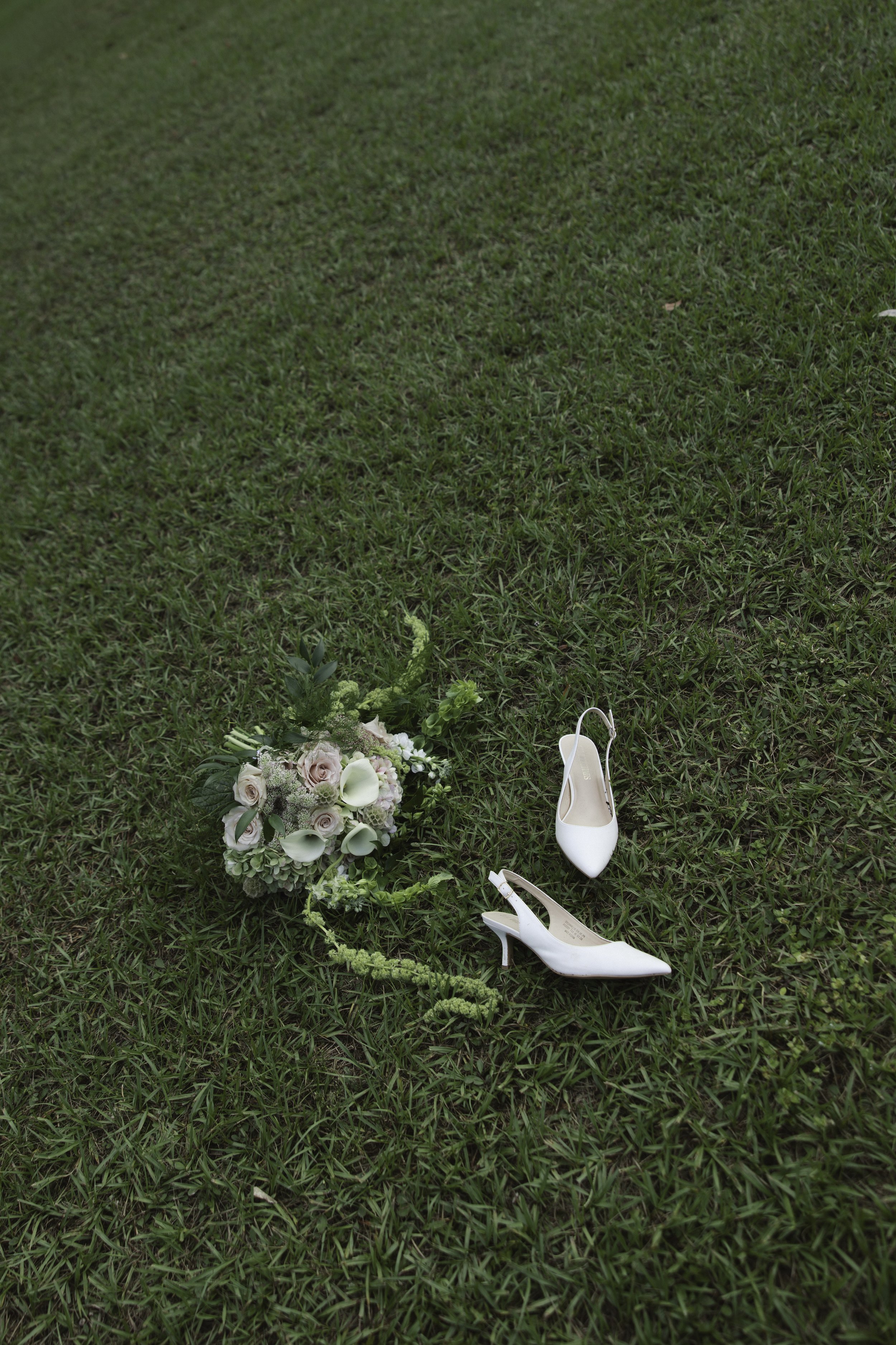 Wedding bouquet and white high-heeled shoes on grass.