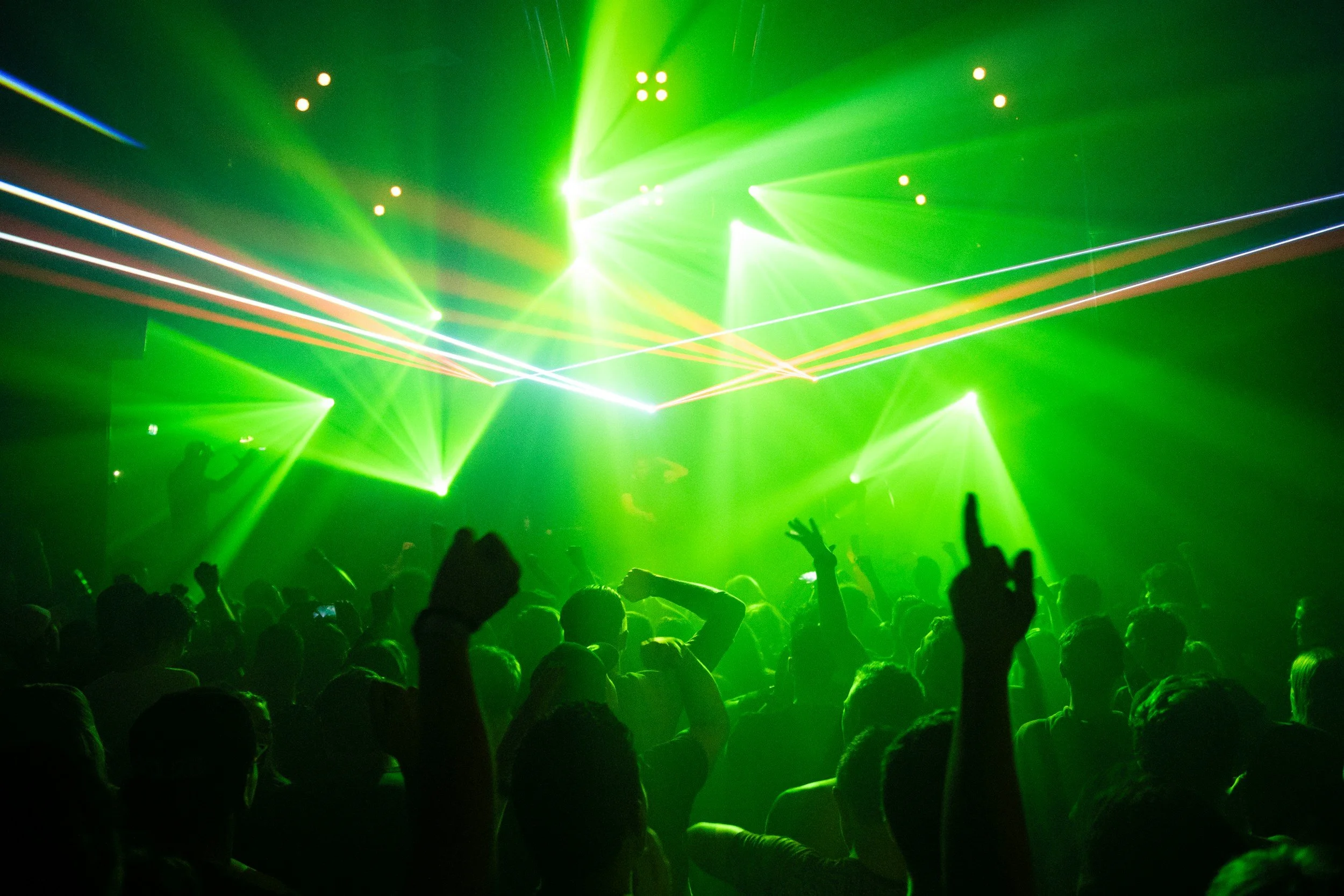 Crowd of people at a concert or nightclub with green laser lights and stage lighting.
