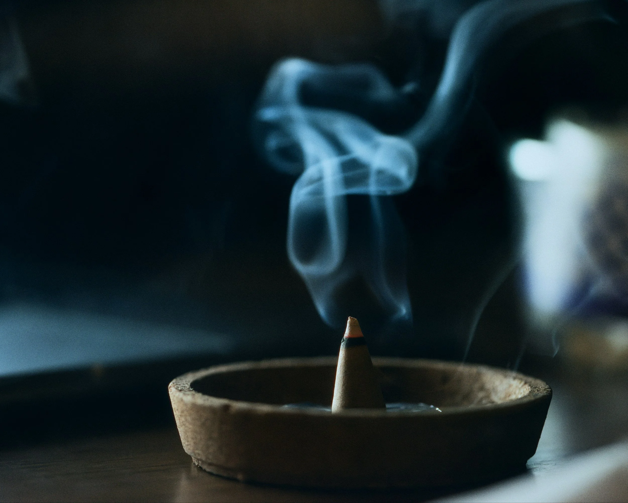 A ceramic incense holder with a cone-shaped incense stick burning and releasing smoke.