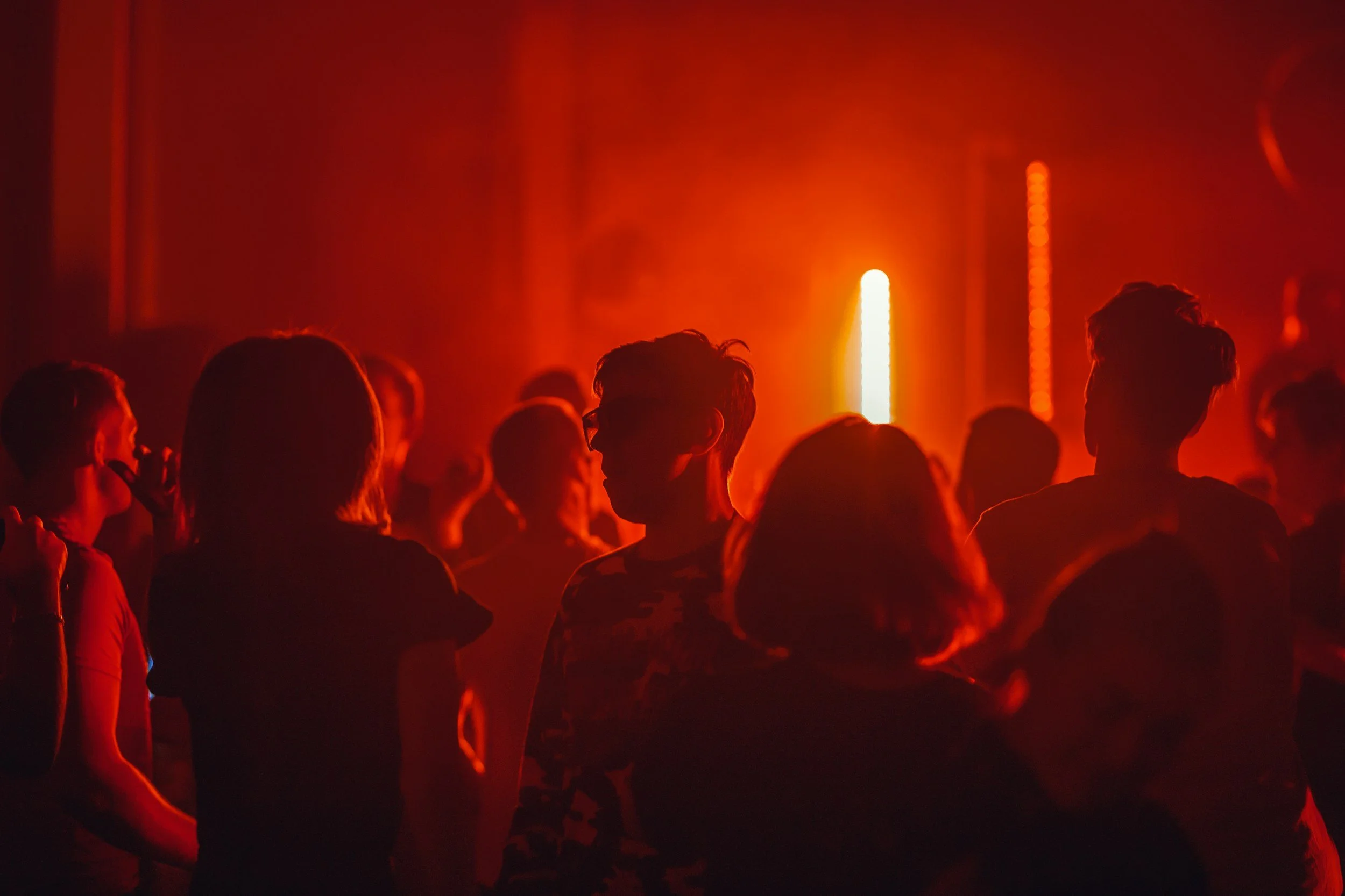 People gathered at a concert or club with red lighting, silhouettes visible in the dark.