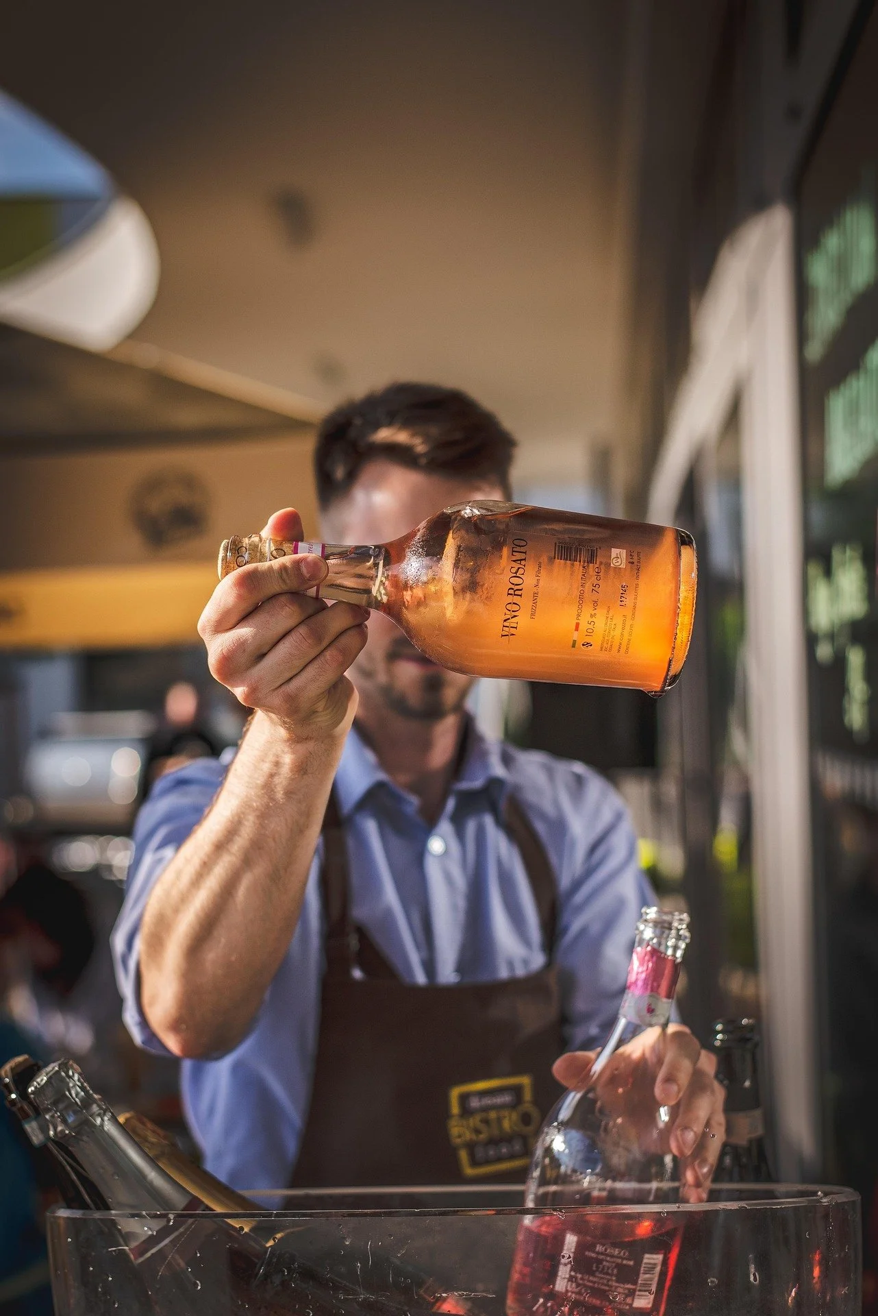 A bartender holding a bottle of Vito Rosato wine, pouring it into a glass at a bar.