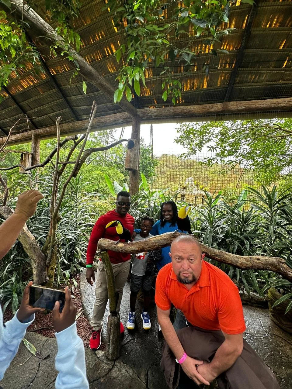 Group of people posing with Toucan bird in indoor jungle exhibit.