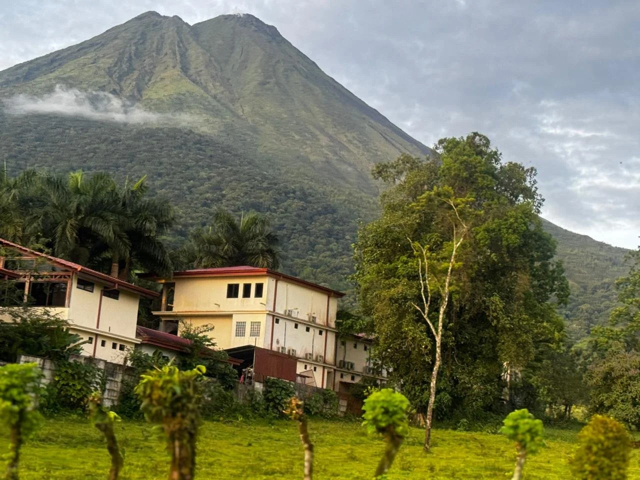 Houses at the base of a large mountain with lush green trees and cloudy sky.