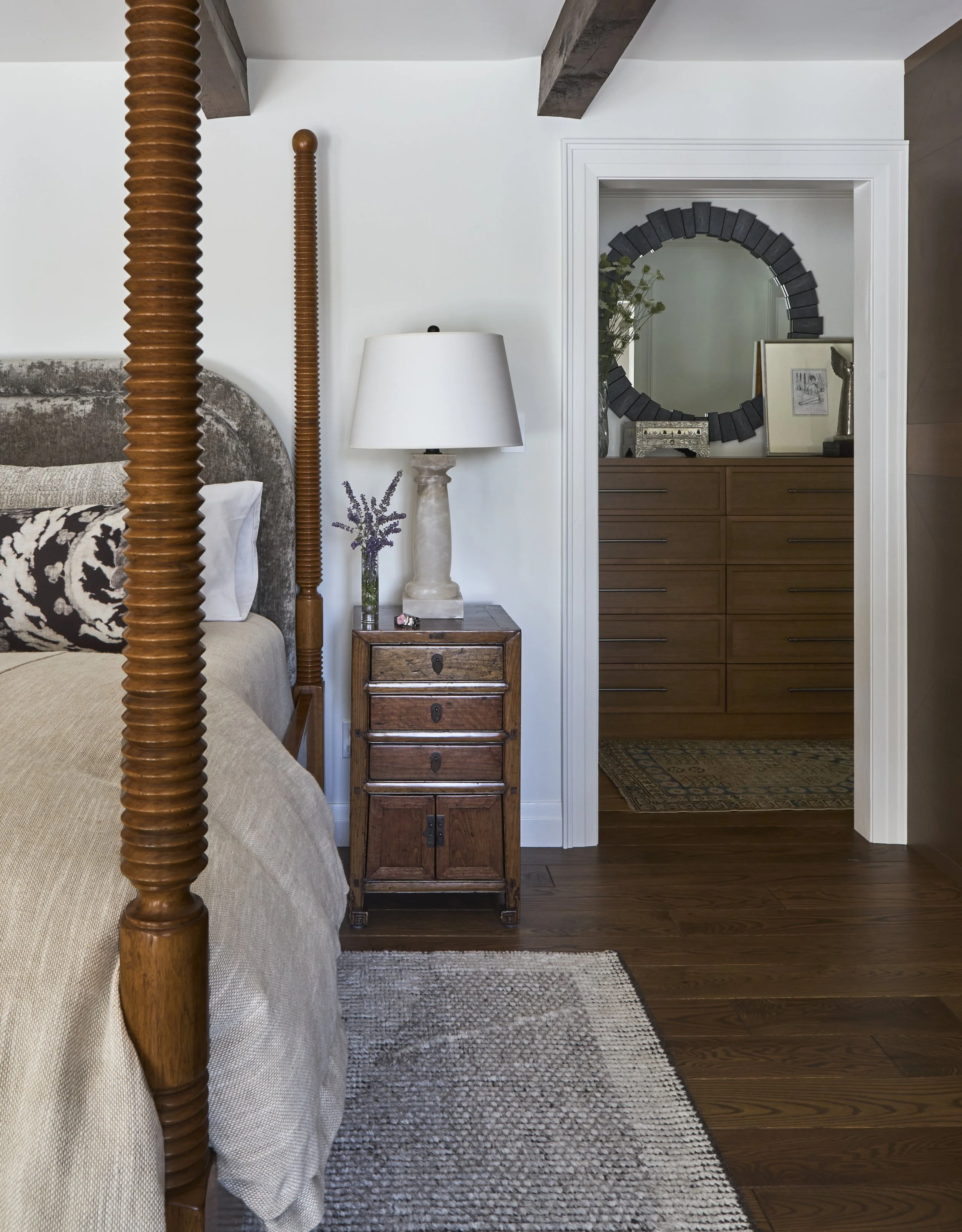Guest ensuite bedroom, dresser in closet. Small nightstand with large bedside lamp. four-poster bed with turned spool legs. hardwood floors in bedroom.