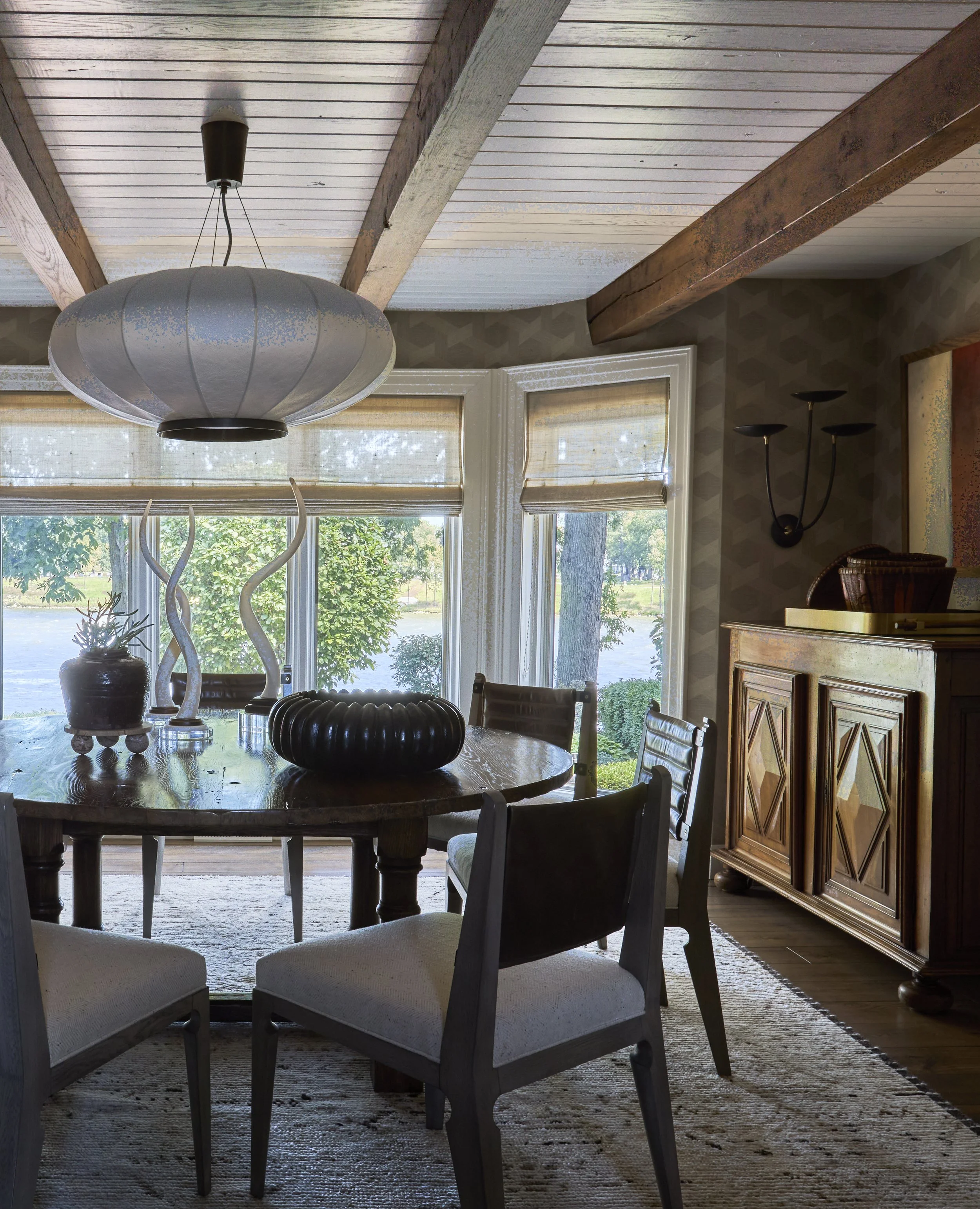 Round dining table with large shade chandelier. Stained ceiling beams with tongue and groove in Dining room.