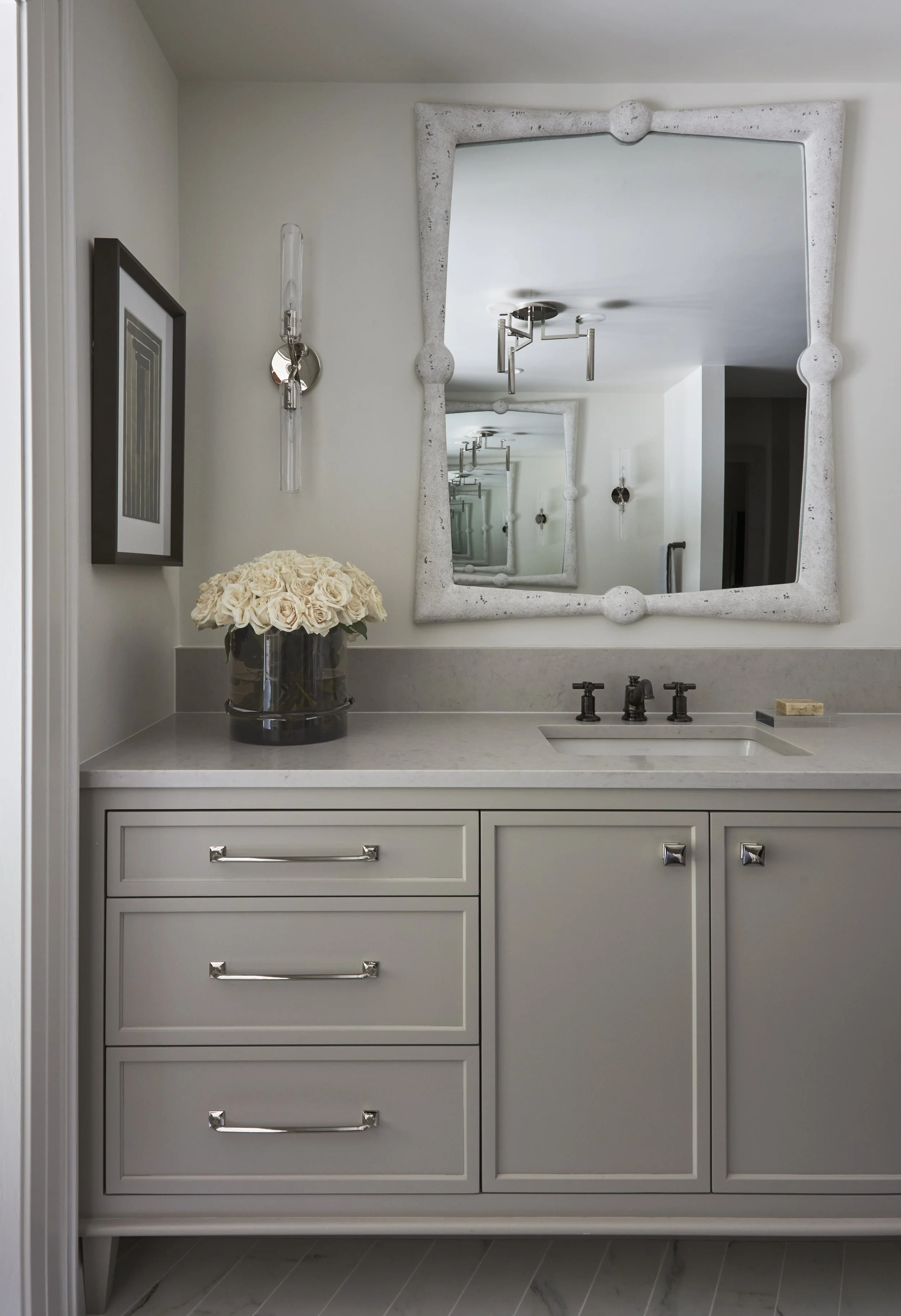Primary bathroom vanity painted gray with light countertops. Polished nickel with dark bronze faucet. Concrete framed mirror.