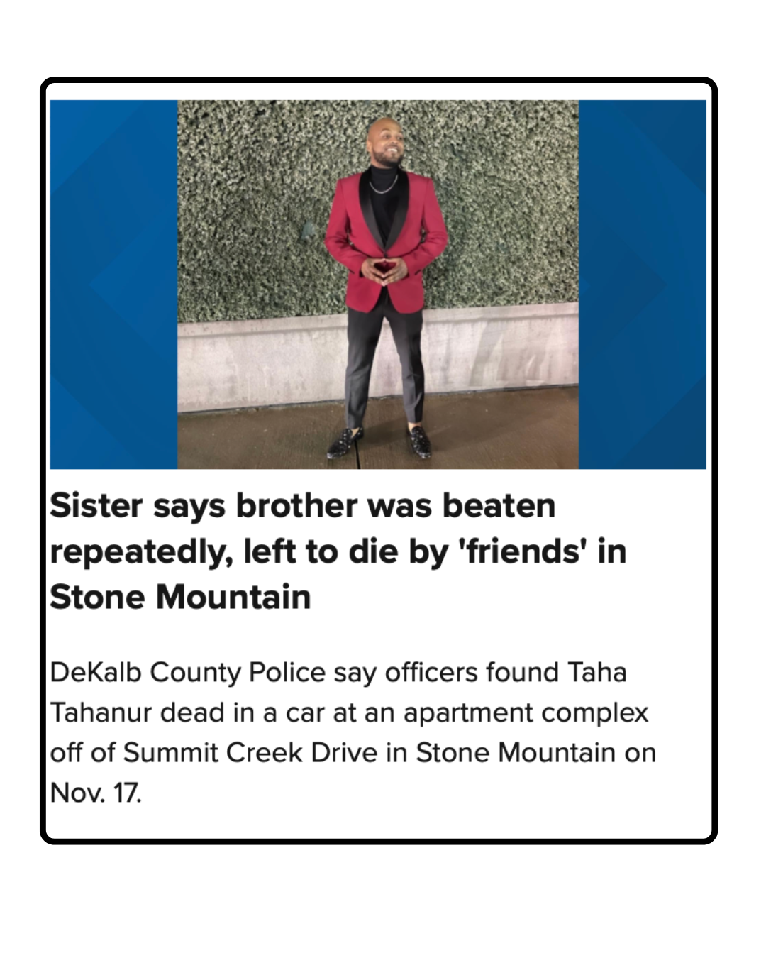 A man dressed in a red blazer, black shirt, and black pants, standing in front of a green plant wall, smiling and holding a phone.