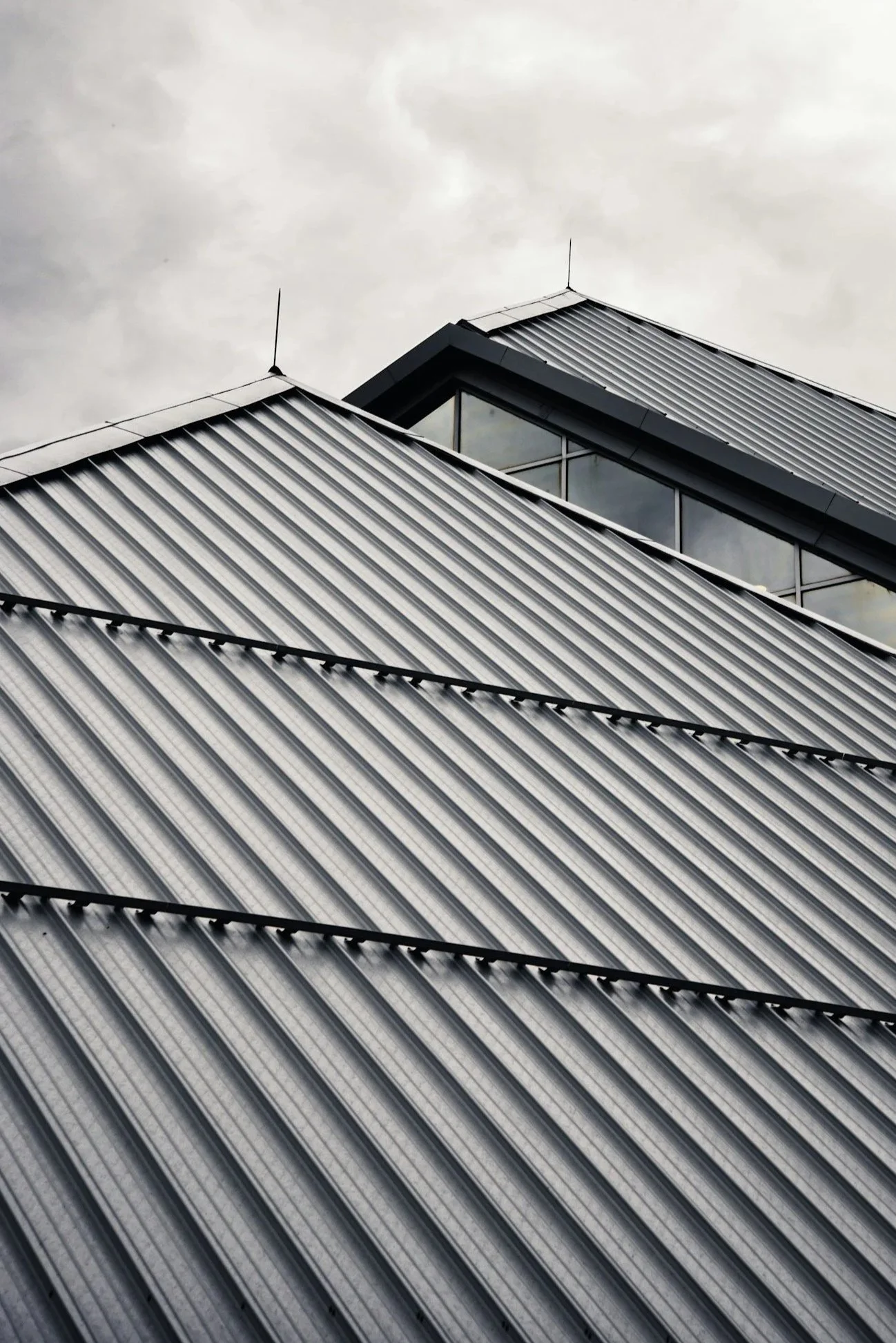 Close-up of modern metal building with sloped roof and glass windows, under gray cloudy sky.