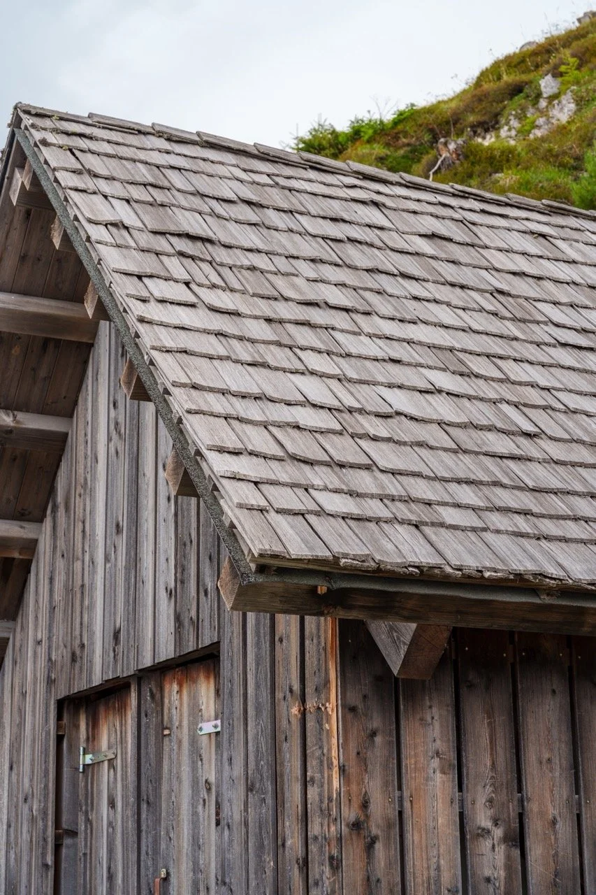 Close-up of a weathered wood barn with a shingled roof on a hillside.