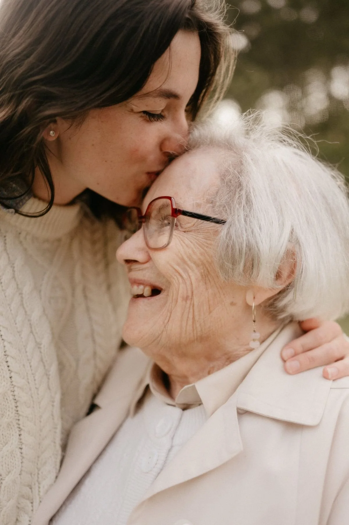 A young woman kissing an elderly woman on the forehead outdoors.