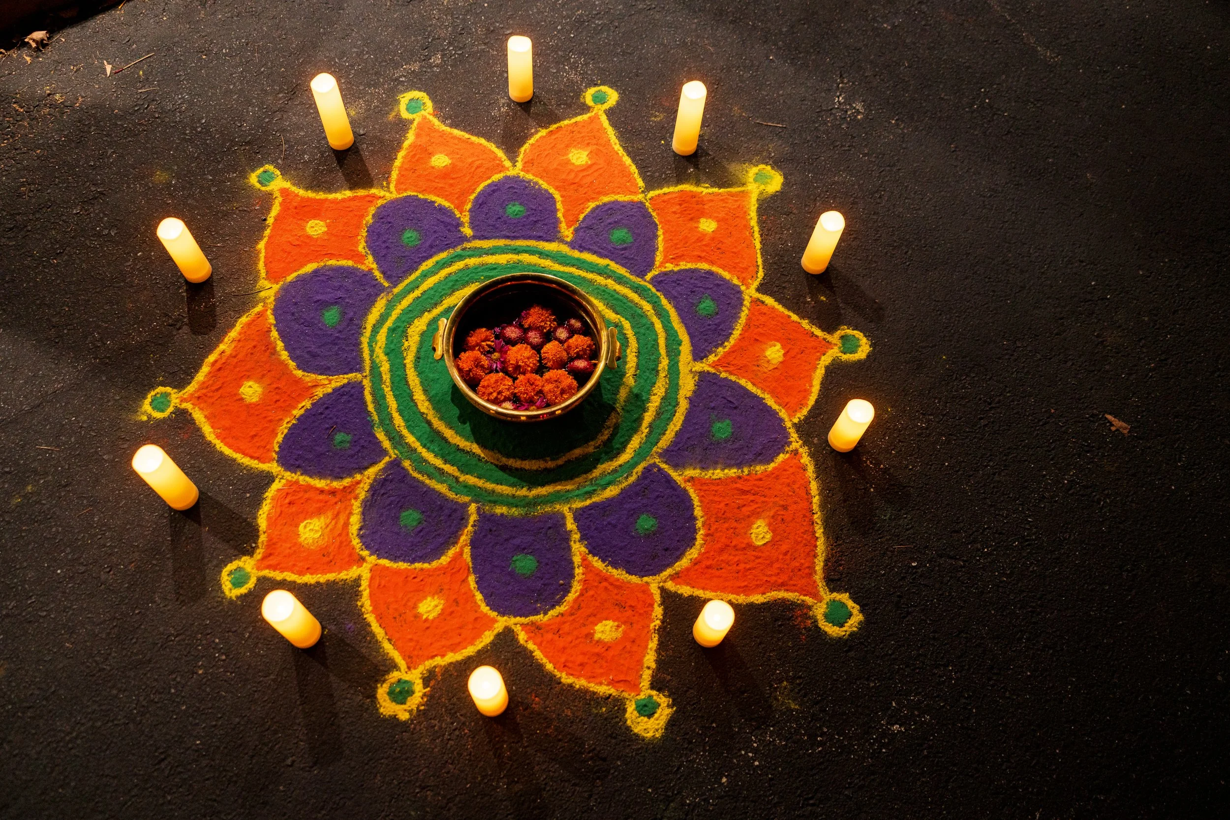 A colorful rangoli design with candles on dark ground.