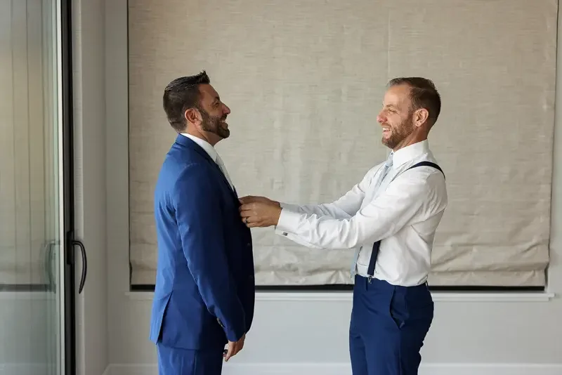 Groom adjusts his tie while getting ready in a modern hotel room on his wedding day.