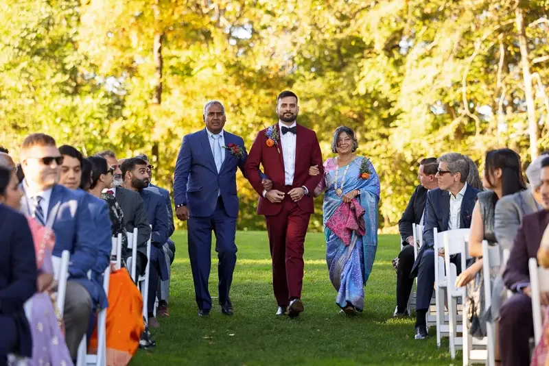 Groom walking down the aisle with his parents during an outdoor fall wedding ceremony