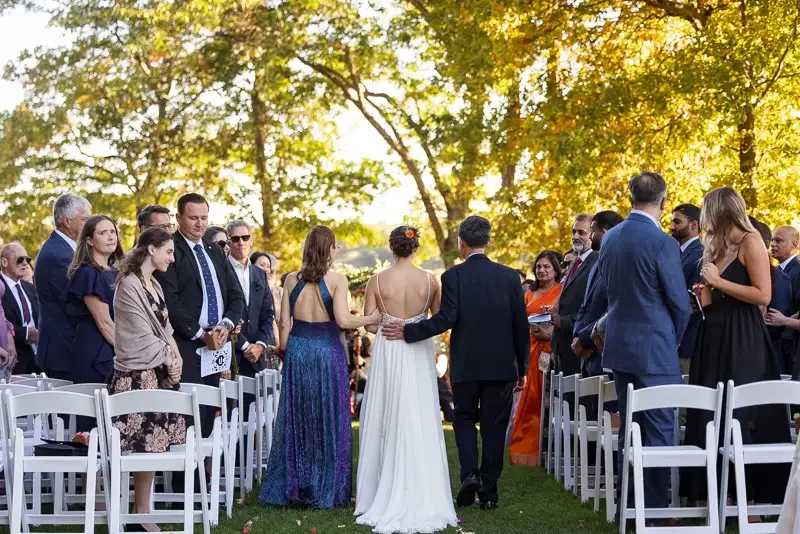 Bride being escorted down the aisle by her parents during an outdoor wedding ceremony