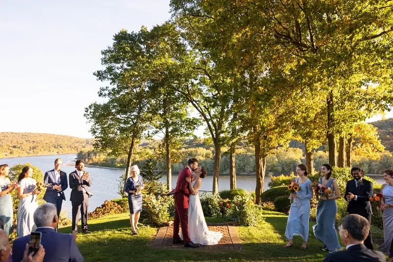 Couple sharing a first kiss at an outdoor riverside wedding ceremony