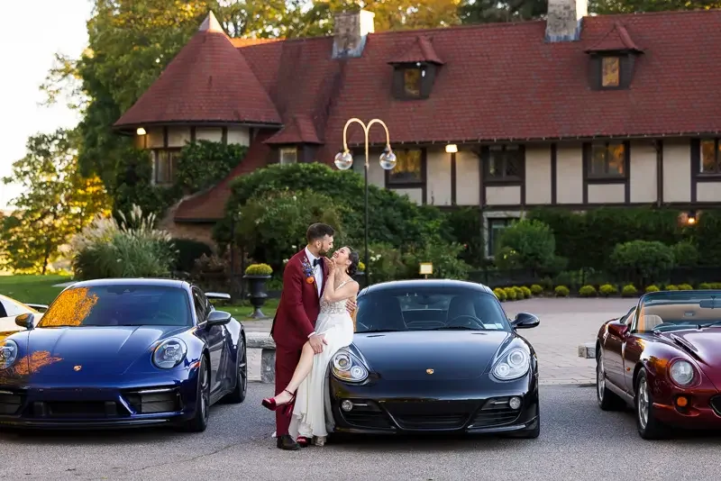 Bride and groom posing in front of Saint Clements Castle with luxury cars