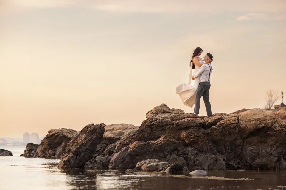 Groom lifting bride on rocky coastline at golden hour