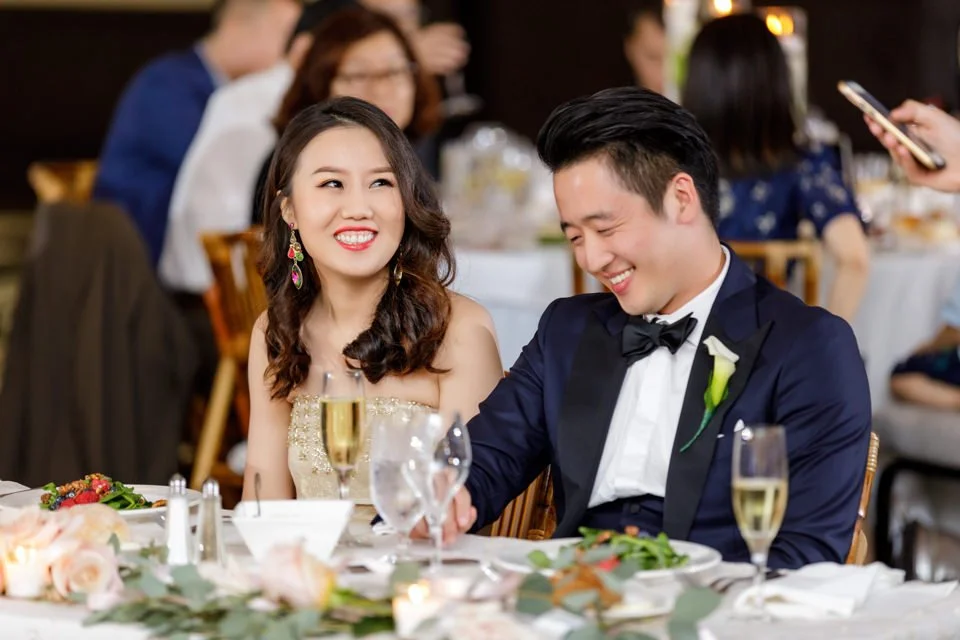 28-couple-seated-reception-table-facing-smiling.jpg