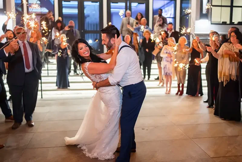 Joyful wedding sparkler exit with a newlywed couple laughing and embracing as guests celebrate around them.