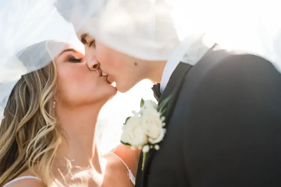 Bride and groom share an intimate kiss under the veil during a romantic wedding portrait.