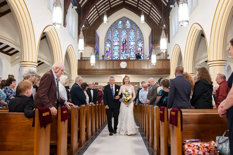 A bride walking down the aisle surrounded by attentive guests, capturing a meaningful and distraction-free ceremony moment.