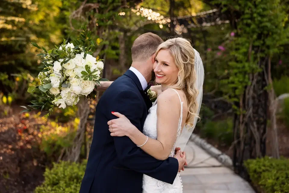 Bride smiling as she embraces her groom during a candid garden wedding portrait in soft natural light.