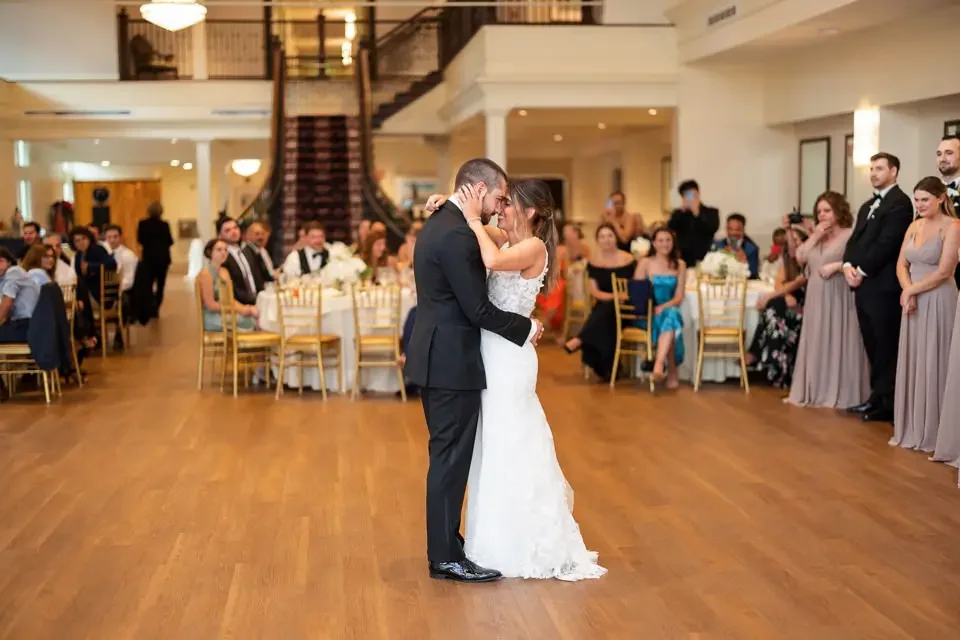 Bride and groom share an intimate first dance surrounded by guests during an elegant wedding reception.