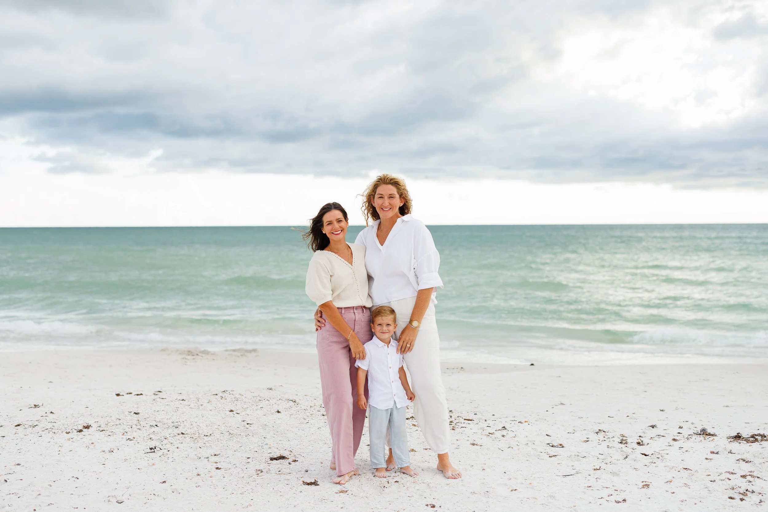 Three people smiling on a beach with ocean behind them.