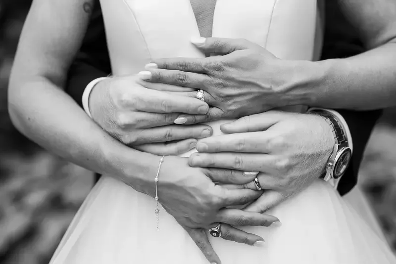 Candid close-up of a bride and groom holding each other, highlighting hands, rings, and connection.
